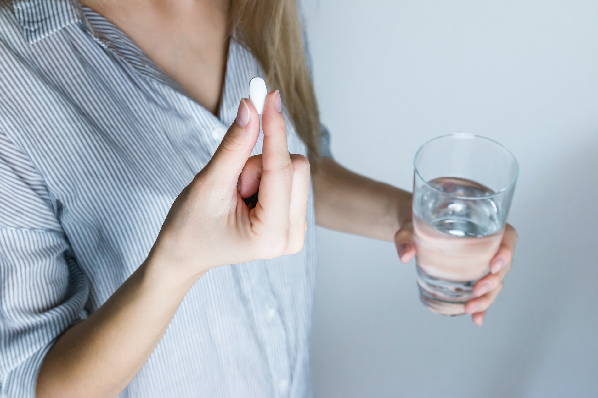 This picture shows a woman neck down, holding a glas of water and a pill