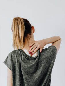 This picture shows a woman from behind, touching her neck as if in pain